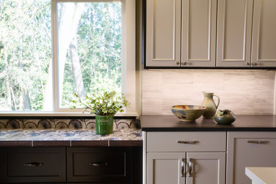 Eat-in kitchen - mid-sized transitional l-shaped medium tone wood floor eat-in kitchen idea in Seattle with a farmhouse sink, recessed-panel cabinets, black cabinets, quartz countertops, multicolored backsplash, stone tile backsplash, stainless steel appliances and an island
