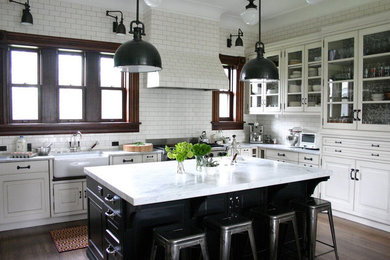 Example of a large transitional l-shaped dark wood floor and brown floor eat-in kitchen design in Other with a farmhouse sink, raised-panel cabinets, white cabinets, marble countertops, white backsplash, subway tile backsplash, stainless steel appliances and an island