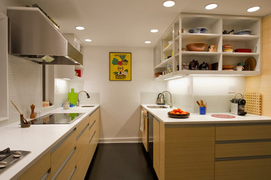 Example of a mid-sized minimalist galley dark wood floor and black floor kitchen design in Boston with flat-panel cabinets, light wood cabinets, solid surface countertops, white backsplash, glass tile backsplash, an undermount sink and stainless steel appliances