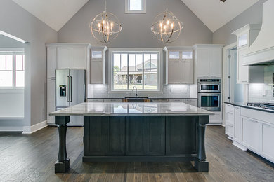 Inspiration for a large transitional l-shaped dark wood floor and brown floor kitchen remodel in Other with a farmhouse sink, shaker cabinets, white cabinets, stainless steel appliances, an island, quartz countertops, white backsplash, subway tile backsplash and gray countertops