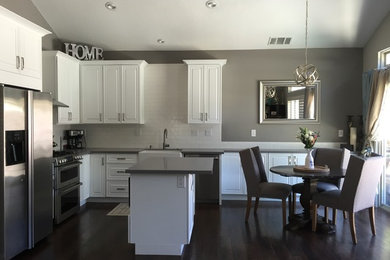Kitchen - transitional l-shaped dark wood floor kitchen idea in San Francisco with a farmhouse sink, raised-panel cabinets, white cabinets, quartz countertops, white backsplash, subway tile backsplash, stainless steel appliances and an island