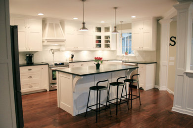 Example of a mid-sized transitional l-shaped dark wood floor and brown floor open concept kitchen design in Philadelphia with a farmhouse sink, shaker cabinets, white cabinets, solid surface countertops, white backsplash, subway tile backsplash, stainless steel appliances and an island