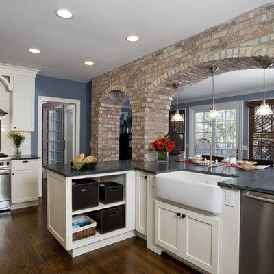 Eat-in kitchen - mid-sized traditional u-shaped medium tone wood floor and brown floor eat-in kitchen idea in Chicago with stainless steel appliances, subway tile backsplash, a farmhouse sink, soapstone countertops, shaker cabinets, white cabinets, white backsplash and black countertops