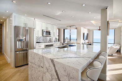 Small trendy galley light wood floor and beige floor open concept kitchen photo in Miami with a double-bowl sink, white cabinets, stainless steel appliances, an island, shaker cabinets, marble countertops, gray backsplash and matchstick tile backsplash