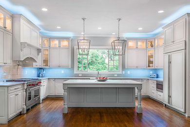 Example of a huge classic u-shaped medium tone wood floor and brown floor eat-in kitchen design in DC Metro with a farmhouse sink, raised-panel cabinets, white cabinets, quartz countertops, gray backsplash, glass tile backsplash, stainless steel appliances, an island and white countertops