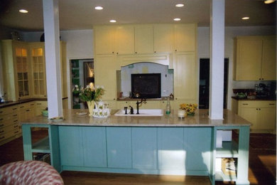 Inspiration for a mid-sized timeless medium tone wood floor enclosed kitchen remodel in Other with a drop-in sink, flat-panel cabinets, yellow cabinets, stainless steel appliances and an island