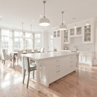 Photo of a traditional eat-in kitchen in New York with glass-front cabinets, marble benchtops, white splashback, stone slab splashback and white cabinets.