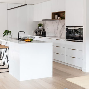 Diseño de cocina de galera, minimalista, de tamaño medio, abierta, con fregadero de doble seno, puertas de armario blancas, encimera de cuarzo compacto, salpicadero blanco, salpicadero de mármol, electrodomésticos blancos, suelo laminado, una isla, suelo marrón y encimeras blancas