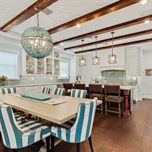 Photo of a large tropical eat-in kitchen in Tampa with a farmhouse sink, louvered cabinets, white cabinets, granite benchtops, blue splashback, glass tile splashback, stainless steel appliances, medium hardwood floors, with island, brown floor, beige benchtop and exposed beam.