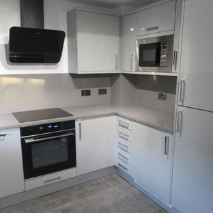 Small modern u-shaped eat-in kitchen in Other with an undermount sink, flat-panel cabinets, grey cabinets, quartzite benchtops, glass sheet splashback, black appliances, vinyl floors, no island, grey floor and grey benchtop.
