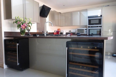 This is an example of a large contemporary u-shaped kitchen/diner in Essex with a single-bowl sink, flat-panel cabinets, laminate countertops, beige splashback, glass sheet splashback, black appliances and ceramic flooring.