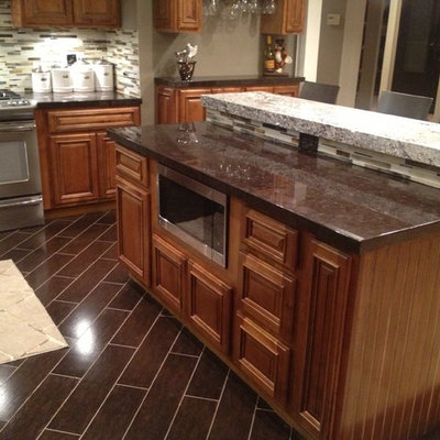 Inspiration for a mid-sized transitional single-wall dark wood floor and brown floor eat-in kitchen remodel in Orange County with raised-panel cabinets, medium tone wood cabinets, granite countertops, multicolored backsplash, matchstick tile backsplash, stainless steel appliances, an island and black countertops