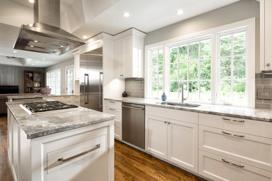 Example of a large trendy l-shaped medium tone wood floor eat-in kitchen design in Kansas City with a drop-in sink, recessed-panel cabinets, white cabinets, granite countertops, gray backsplash, glass tile backsplash, stainless steel appliances and an island