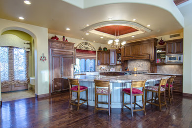 Inspiration for a timeless u-shaped dark wood floor open concept kitchen remodel in Phoenix with a farmhouse sink, raised-panel cabinets, dark wood cabinets, granite countertops, beige backsplash, stone tile backsplash, paneled appliances and an island