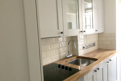 Design ideas for a small single-wall enclosed kitchen in London with a built-in sink, recessed-panel cabinets, grey cabinets, wood worktops, beige splashback, ceramic splashback, stainless steel appliances, ceramic flooring, a breakfast bar, grey floors and brown worktops.