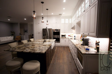 Large transitional l-shaped dark wood floor open concept kitchen photo in Miami with a farmhouse sink, raised-panel cabinets, dark wood cabinets, granite countertops, white backsplash, porcelain backsplash, stainless steel appliances and an island