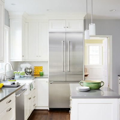 Example of a mid-sized transitional u-shaped dark wood floor and brown floor enclosed kitchen design in DC Metro with shaker cabinets, white cabinets, white backsplash, an island, a farmhouse sink, solid surface countertops, subway tile backsplash and stainless steel appliances