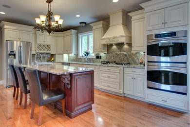 Example of a mid-sized classic l-shaped medium tone wood floor and brown floor kitchen design in Other with a double-bowl sink, raised-panel cabinets, white cabinets, granite countertops, brown backsplash, stone slab backsplash, stainless steel appliances and an island