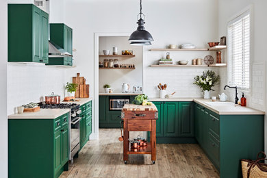 Foto på ett vintage beige u-kök, med en nedsänkt diskho, luckor med upphöjd panel, gröna skåp, träbänkskiva, vitt stänkskydd, stänkskydd i tunnelbanekakel, rostfria vitvaror, mellanmörkt trägolv, en köksö och brunt golv