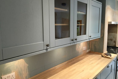Photo of a medium sized modern galley kitchen/diner in London with a belfast sink, recessed-panel cabinets, blue cabinets, wood worktops, metallic splashback, metal splashback, black appliances and ceramic flooring.