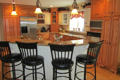 Example of a mid-sized classic l-shaped light wood floor eat-in kitchen design in Providence with a double-bowl sink, medium tone wood cabinets, granite countertops, stainless steel appliances, raised-panel cabinets, yellow backsplash and an island