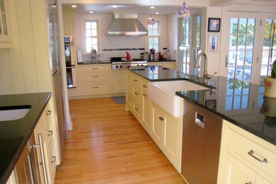Example of a mid-sized classic single-wall light wood floor kitchen design in Bridgeport with yellow cabinets, white backsplash, subway tile backsplash, stainless steel appliances and an island