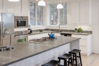 Photo of a large contemporary u-shaped kitchen/diner in Portland Maine with a submerged sink, flat-panel cabinets, white cabinets, marble worktops, stainless steel appliances, light hardwood flooring and an island.