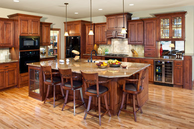 Large elegant l-shaped light wood floor and brown floor kitchen photo in Milwaukee with black appliances, raised-panel cabinets, medium tone wood cabinets, beige backsplash, an island, an undermount sink and granite countertops