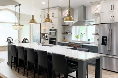 Example of a large transitional galley light wood floor, brown floor and vaulted ceiling eat-in kitchen design in Other with an undermount sink, shaker cabinets, white cabinets, quartzite countertops, white backsplash, ceramic backsplash, stainless steel appliances, an island and white countertops