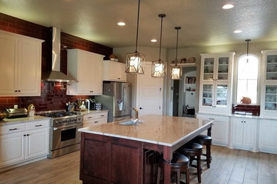 Large transitional l-shaped light wood floor and brown floor kitchen photo in Austin with an undermount sink, raised-panel cabinets, white cabinets, quartzite countertops, red backsplash, glass tile backsplash, stainless steel appliances and an island