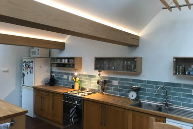 Photo of a medium sized contemporary u-shaped kitchen in Hampshire with an integrated sink, light wood cabinets, wood worktops, grey splashback, stone tiled splashback, white appliances, slate flooring, grey floors, exposed beams and an island.