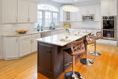 Inspiration for a large contemporary l-shaped medium tone wood floor eat-in kitchen remodel in Boston with a drop-in sink, raised-panel cabinets, white cabinets, granite countertops, white backsplash, ceramic backsplash, stainless steel appliances and an island