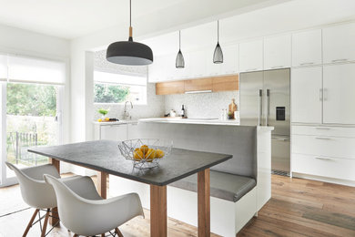 Example of a mid-sized trendy l-shaped medium tone wood floor eat-in kitchen design in Toronto with an undermount sink, flat-panel cabinets, white cabinets, multicolored backsplash, mosaic tile backsplash, stainless steel appliances, an island, white countertops and quartz countertops
