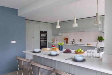 Inspiration for a contemporary u-shaped kitchen/diner in Gloucestershire with an integrated sink, shaker cabinets, green cabinets, quartz worktops, white splashback, ceramic splashback, black appliances, vinyl flooring, a breakfast bar, grey floors and white worktops.