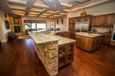 Large tuscan dark wood floor eat-in kitchen photo in Las Vegas with an undermount sink, shaker cabinets, brown cabinets, granite countertops, brown backsplash, stone tile backsplash, stainless steel appliances and two islands