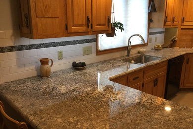 Example of a mid-sized classic u-shaped porcelain tile eat-in kitchen design in Other with an undermount sink, raised-panel cabinets, light wood cabinets, granite countertops, white backsplash, ceramic backsplash, black appliances and no island