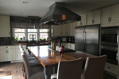 Photo of a large farmhouse galley kitchen/diner in Chicago with a belfast sink, recessed-panel cabinets, distressed cabinets, wood worktops, grey splashback, stone tiled splashback, stainless steel appliances, ceramic flooring, an island, brown floors and brown worktops.