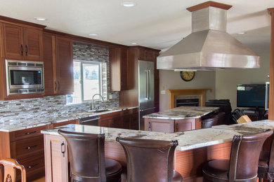 Photo of a medium sized traditional galley open plan kitchen in Seattle with a submerged sink, recessed-panel cabinets, medium wood cabinets, marble worktops, beige splashback, glass tiled splashback, stainless steel appliances, medium hardwood flooring, multiple islands and brown floors.