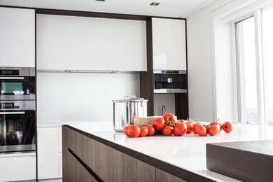 Example of a mid-sized trendy dark wood floor enclosed kitchen design in Montreal with solid surface countertops, white backsplash, stainless steel appliances, an island, flat-panel cabinets and white cabinets