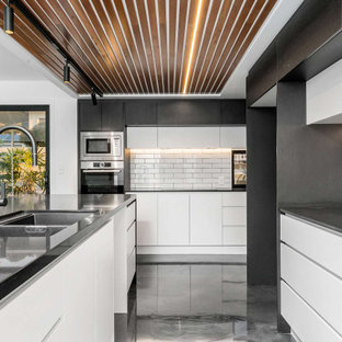 Large contemporary kitchen in Gold Coast - Tweed with an undermount sink, flat-panel cabinets, white cabinets, quartz benchtops, white splashback, subway tile splashback, stainless steel appliances, concrete floors, with island, grey floor, black benchtop and wood.