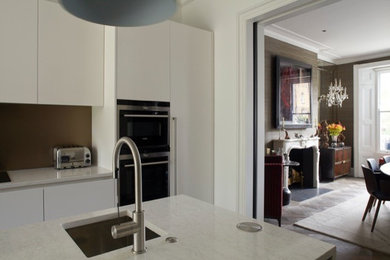 Cette photo montre une cuisine linéaire tendance avec un placard à porte plane, des portes de placard blanches, un plan de travail en quartz modifié, une crédence métallisée, une crédence en feuille de verre et îlot.