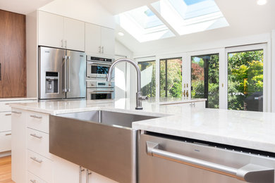 Inspiration for a large traditional l-shaped open plan kitchen in Portland with a submerged sink, flat-panel cabinets, white cabinets, quartz worktops, white splashback, ceramic splashback, stainless steel appliances, medium hardwood flooring and an island.