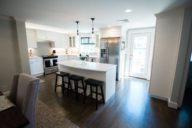 Mid-sized transitional l-shaped dark wood floor and brown floor eat-in kitchen photo in Boston with a farmhouse sink, shaker cabinets, white cabinets, marble countertops, gray backsplash, subway tile backsplash, stainless steel appliances and an island