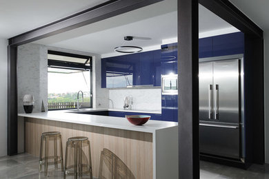 Bild på ett mellanstort funkis kök, med en undermonterad diskho, släta luckor, blå skåp, stänkskydd i marmor, rostfria vitvaror, betonggolv och en halv köksö