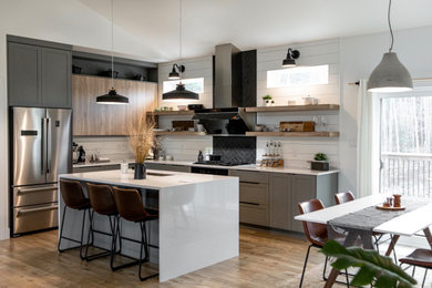 Mid-sized danish l-shaped laminate floor open concept kitchen photo in Other with an undermount sink, shaker cabinets, gray cabinets, solid surface countertops, black backsplash, ceramic backsplash, stainless steel appliances, an island and white countertops