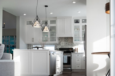 Example of a large classic l-shaped dark wood floor open concept kitchen design in Other with a farmhouse sink, shaker cabinets, white cabinets, solid surface countertops, gray backsplash, cement tile backsplash, stainless steel appliances, an island and white countertops