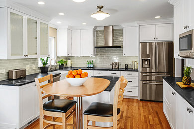 Mid-sized transitional u-shaped medium tone wood floor eat-in kitchen photo in Other with a farmhouse sink, shaker cabinets, white cabinets, onyx countertops, gray backsplash, subway tile backsplash, stainless steel appliances and an island