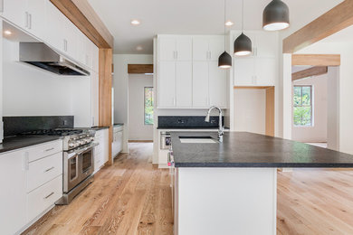 Example of a large minimalist light wood floor kitchen design in Atlanta with flat-panel cabinets, white cabinets, granite countertops, black backsplash, stainless steel appliances and an island