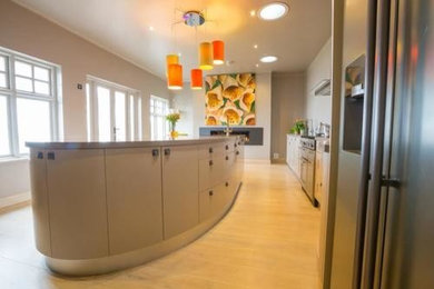 Photo of a contemporary kitchen/diner in Devon with a double-bowl sink, flat-panel cabinets, grey cabinets, composite countertops, stainless steel appliances and an island.