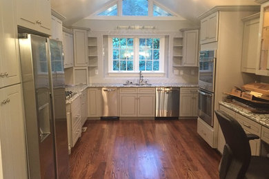 Mid-sized elegant u-shaped medium tone wood floor and brown floor enclosed kitchen photo in Charlotte with a double-bowl sink, granite countertops, ceramic backsplash, no island, white cabinets and stainless steel appliances